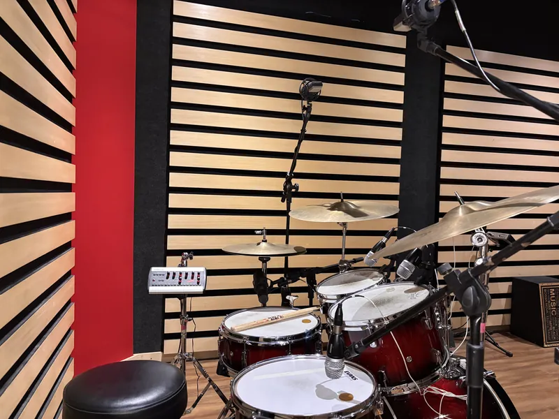 Parede com tratamento acústico ripado na sala de gravação, com a bateria microfonada