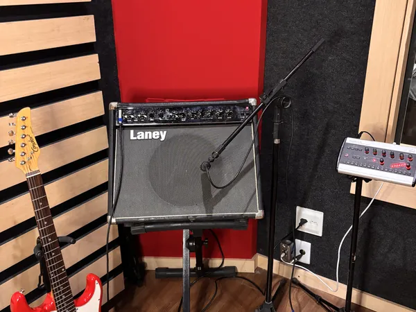 Guitarra, amplificador e microfone posicionados na sala